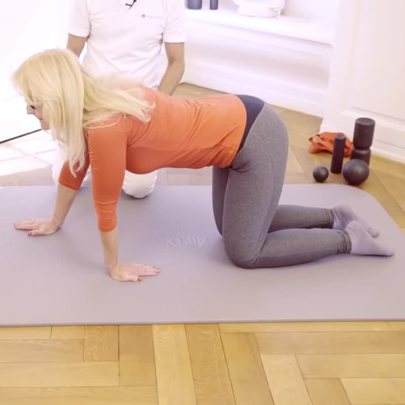 A woman is on her hands and knees stretching her wrist.