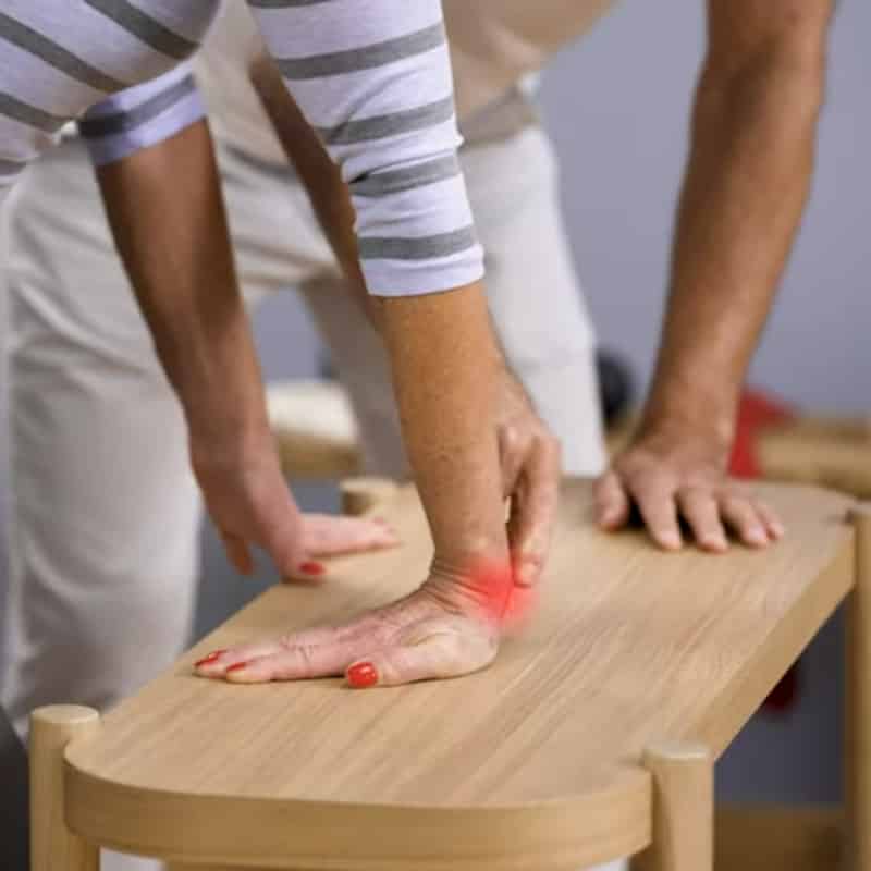 A woman has her hand flat on a table, her fingers are facing her thigh.