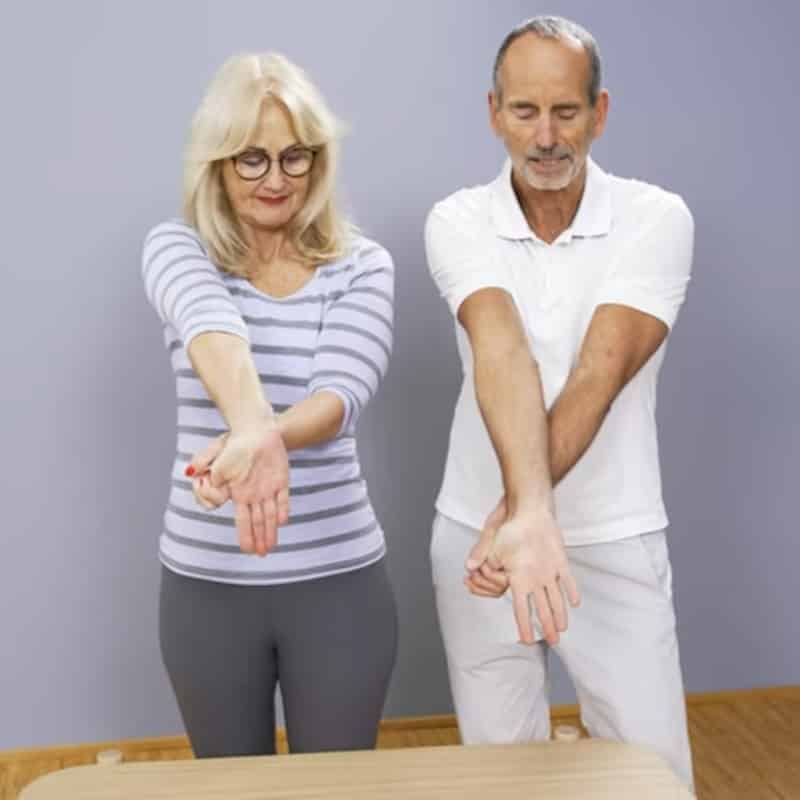 Ina and Roland are flexing their wrists towards the floor and stretching their thumbs.