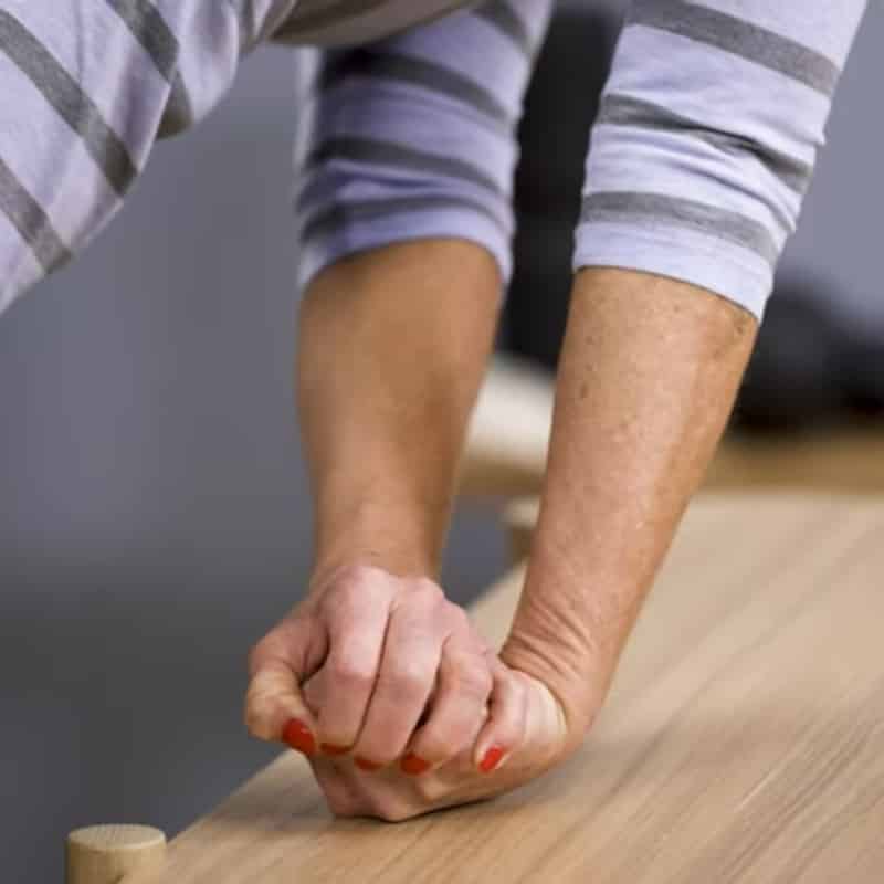 A woman is pressing the back of her fist against a table.