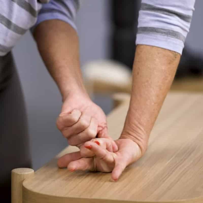A woman is pressing the back of her hand against a table, she's lifting her middle finger with her opposite hand.