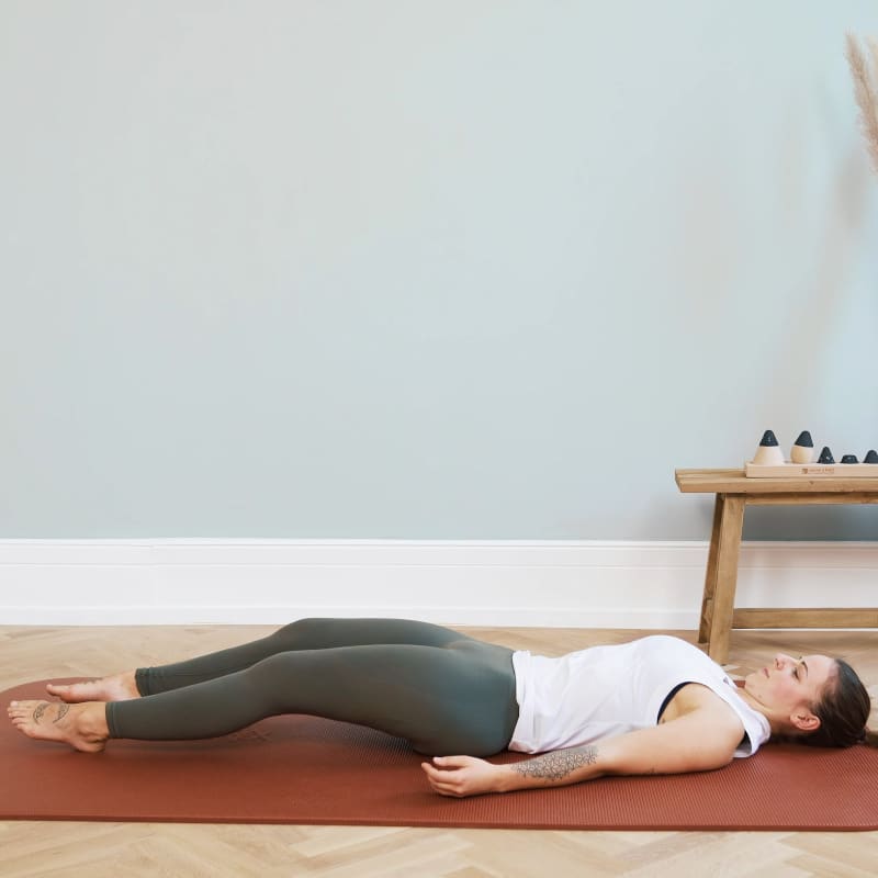 A young woman is lying on the floor, she's pressing her spine against the floor.