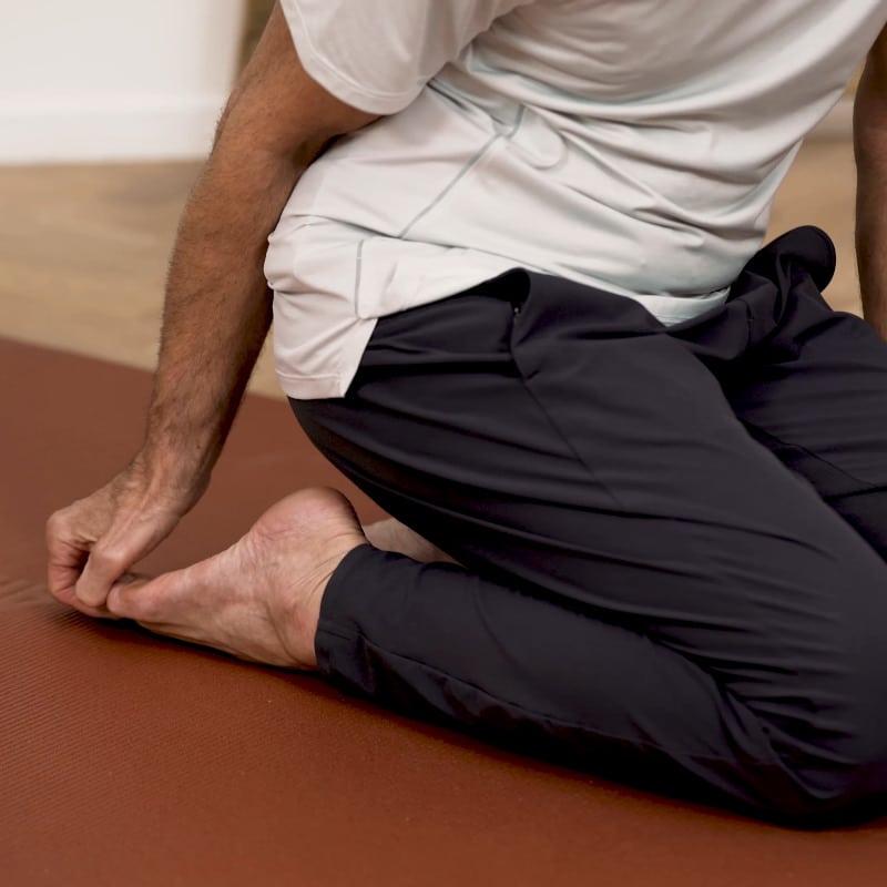 Roland Liebscher-Bracht is sitting on his calves pulling the toes of his right foot.