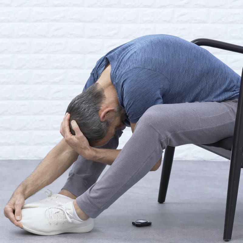 Roland Liebscher-Bracht is sitting in a chair pulling his head down and forward.