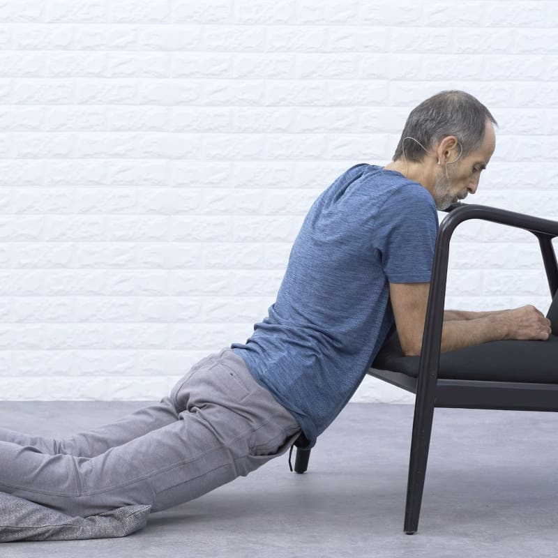 Roland Liebscher-Bracht is leaning his forearms on a chair, his legs are on the floor.