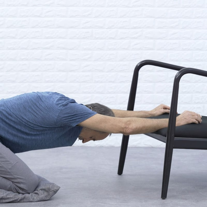 Roland Liebscher-Bracht is sitting back on his heels with his arms resting on the seat of a chair.