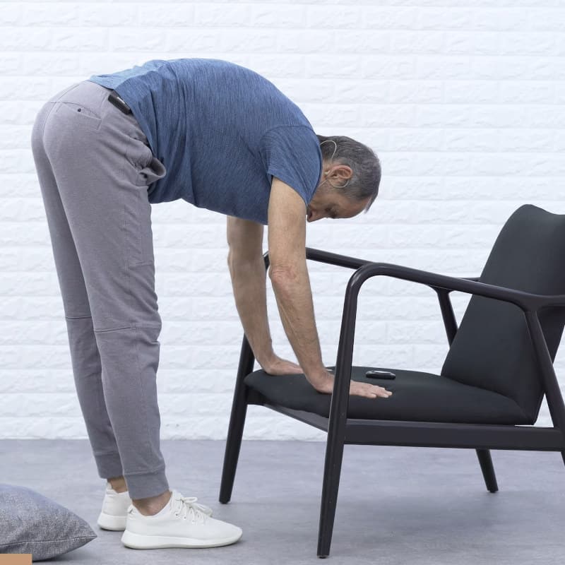 Roland Liebscher-Bracht is bending forward at the waist resting his hands on a chair.