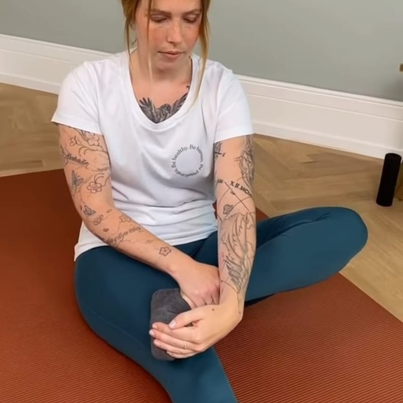 A woman is sitting with her left foot on her right knee, she's pulling her toes into an extension.
