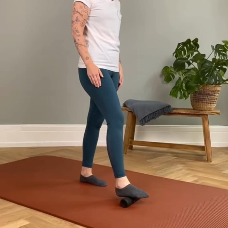 A woman is standing with the Midi Foam Roller under her right foot.