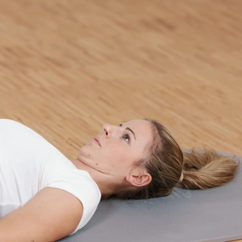 A woman is pressing the back of her neck against the floor.