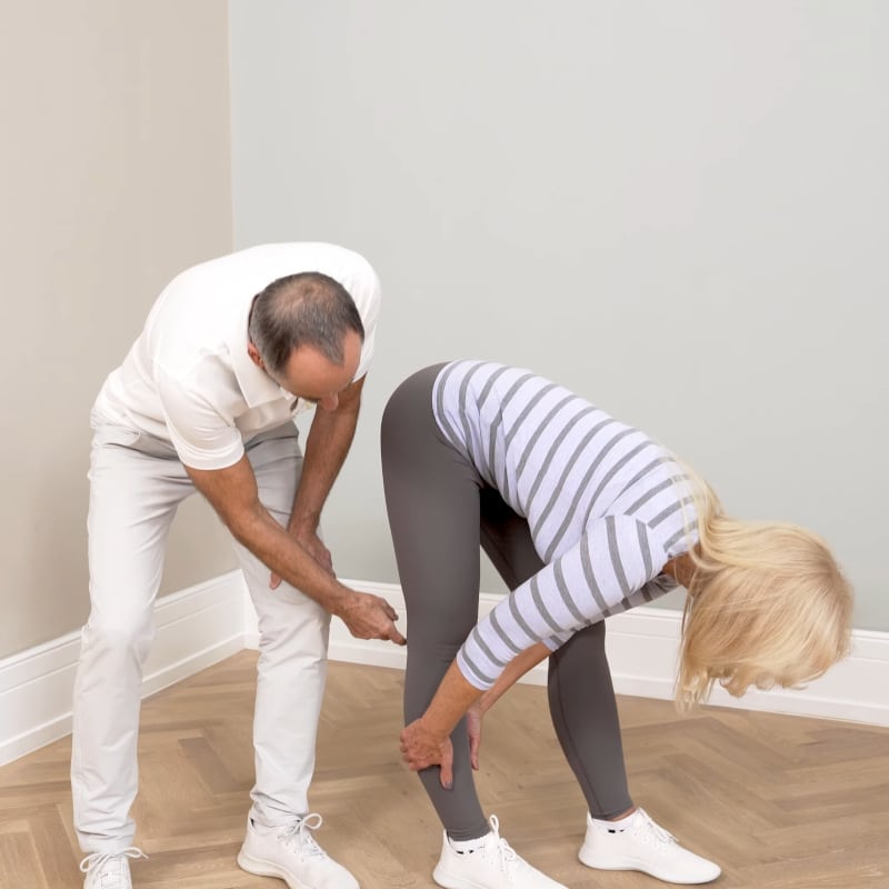 A woman is demonstrating a stretch for Baker's Cyst while Roland Liebscher-Bracht looks on.