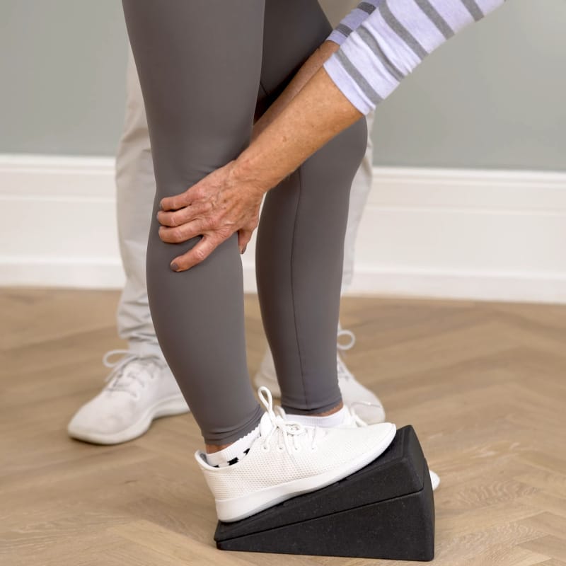 A woman is stretching her knee with the Knee Hero.