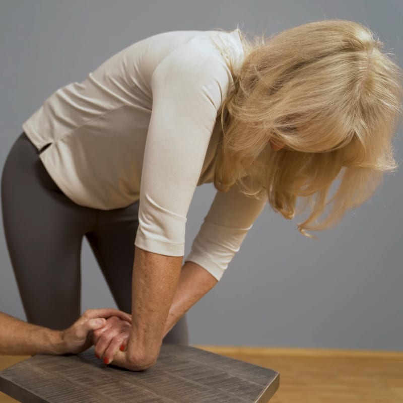 A woman is stretching the top of her wrist on a table.