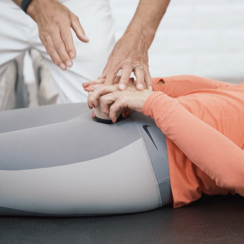 A woman is pressing the Osteopressure tool into her groin as Roland Liebscher-Bracht helps.