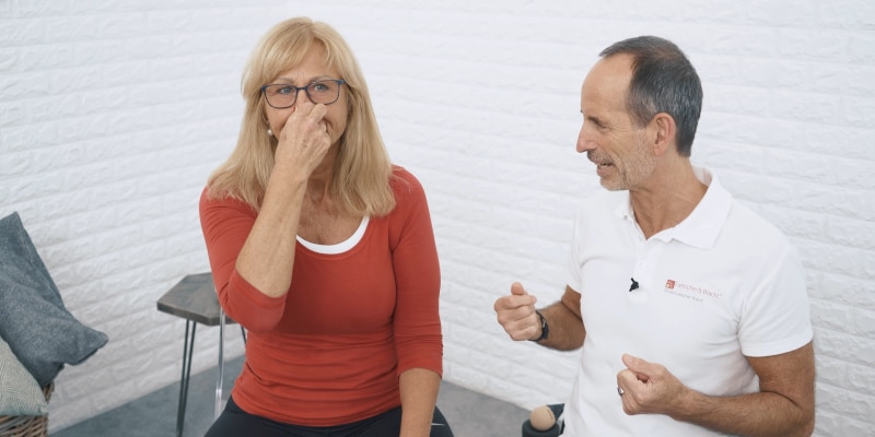 A woman is pinching her nose closed while Roland Liebscher-Bracht looks on.
