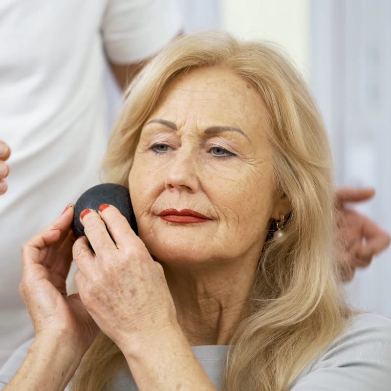 A woman is massaging her jaw with the Mini Massage Ball.