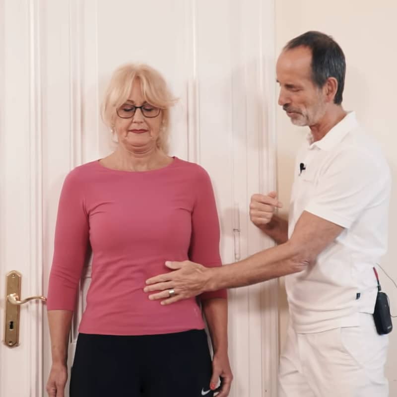 A woman is pressing her back against a wall, Roland Liebscher-Bracht has his hand on her stomach.
