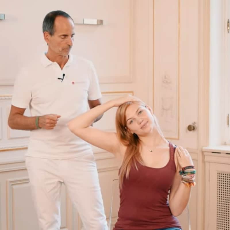 A woman is pulling her right shoulder down and her head to the left while Roland Liebsher-Bracht looks on.