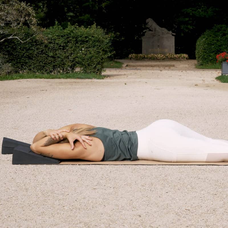 A woman is lying on her stomach with her left arm bent back. She's pressing her hand against her forearm.
