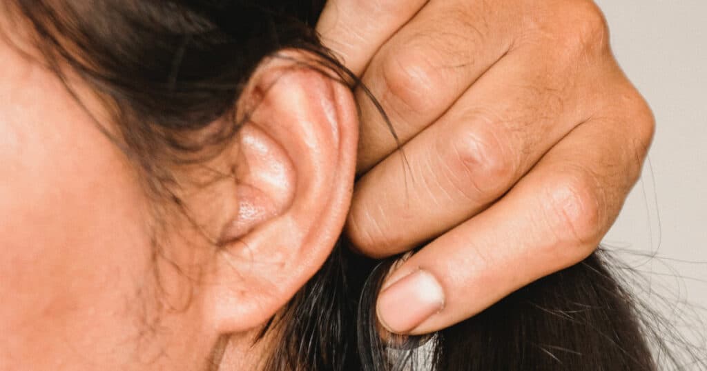 Closeup of a lady pulling back her hair to show her ear.