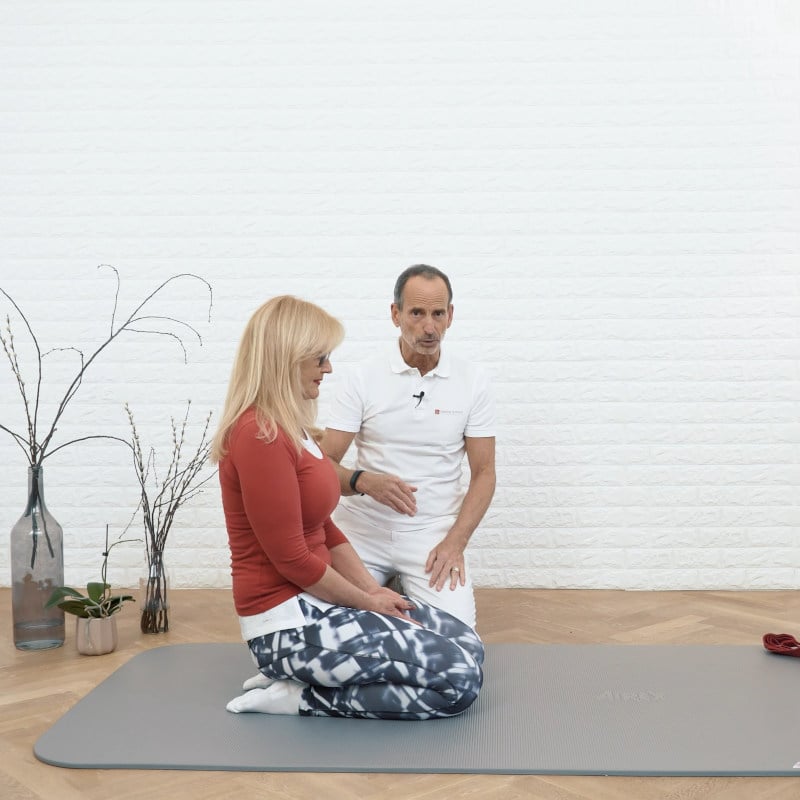 A woman is sitting back on her ankles while Roland Liebscher-Bracht looks on.