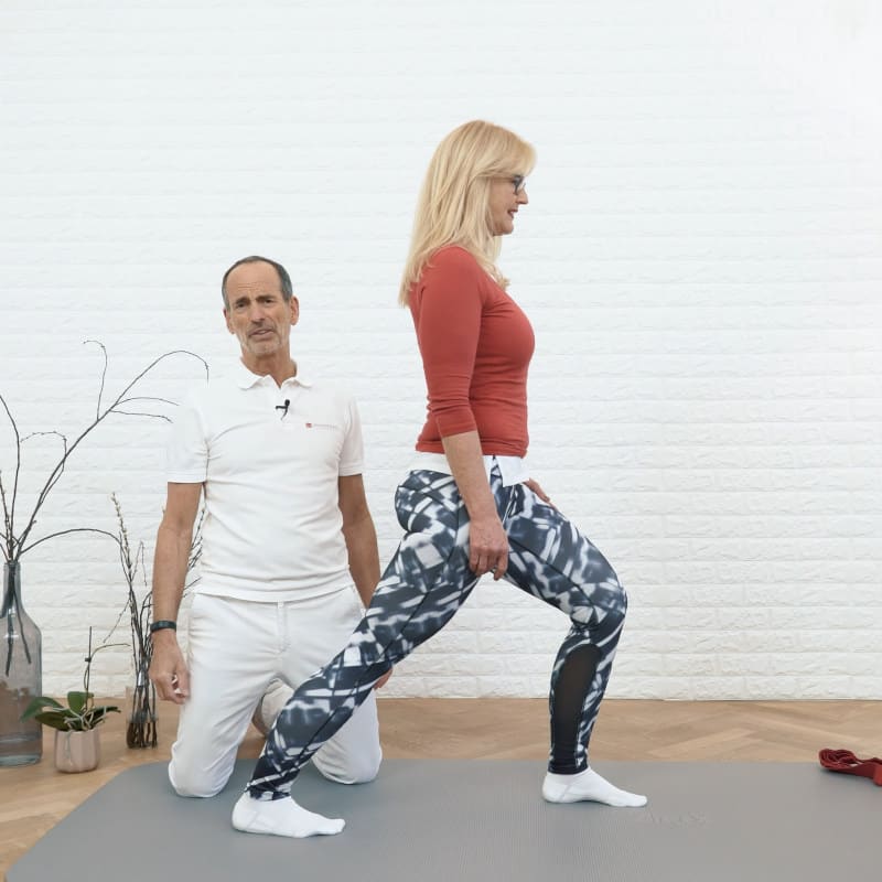 A woman is standing with her back leg stretched while Roland Liebscher-Bracht looks on.
