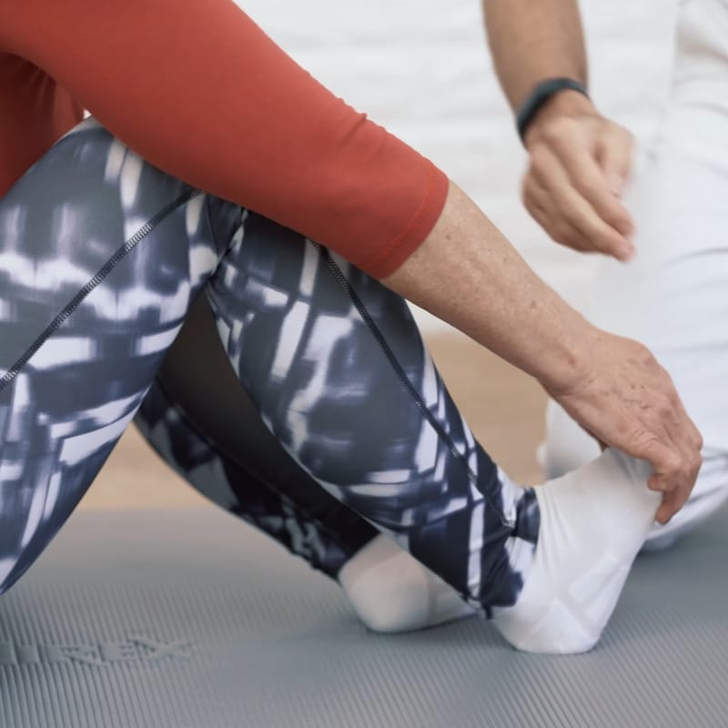 Closeup of someone sitting on the floor with their legs bent pulling the ball of their foot back.