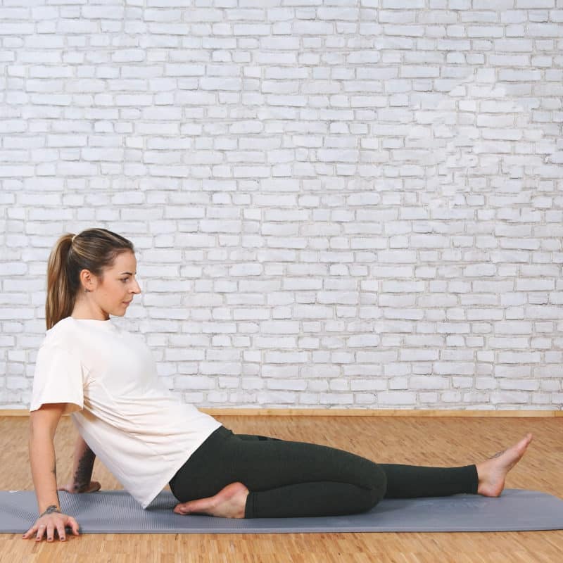 A girl is sitting on the floor with her right leg bent back.