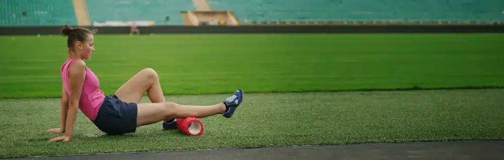 A woman sitting on a field rollmassaging her calf.