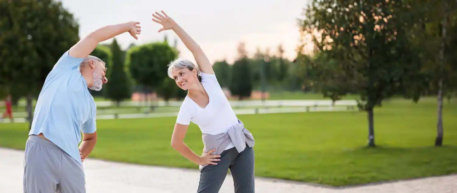 Two elderly people stretching in the park