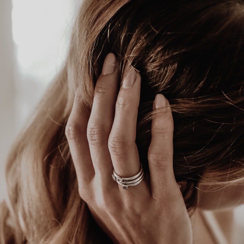 Eine Frau greift mit ihrer Hand in ihr langes braunes Haar. Sie trägt einen Ring und die Fingernägel sind gepflegt.