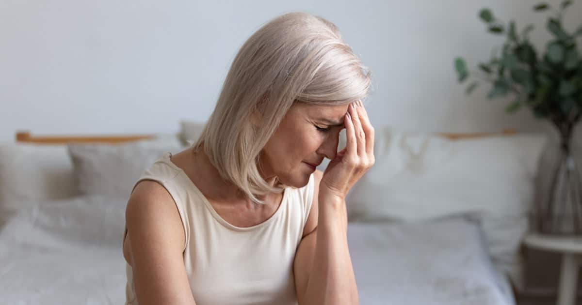 Eine ältere Dame sitzt auf dem Sofa und hält sich mit der linken Hand die Stirn vor Schmerzen