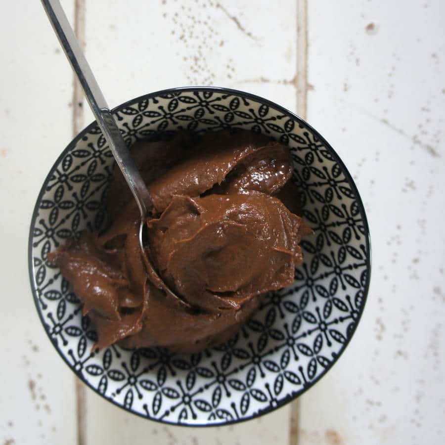 Eine Schüssel mit selbstgemachtem Schokoaufstrich steht auf einem Tisch. Ein Löffel liegt darin.