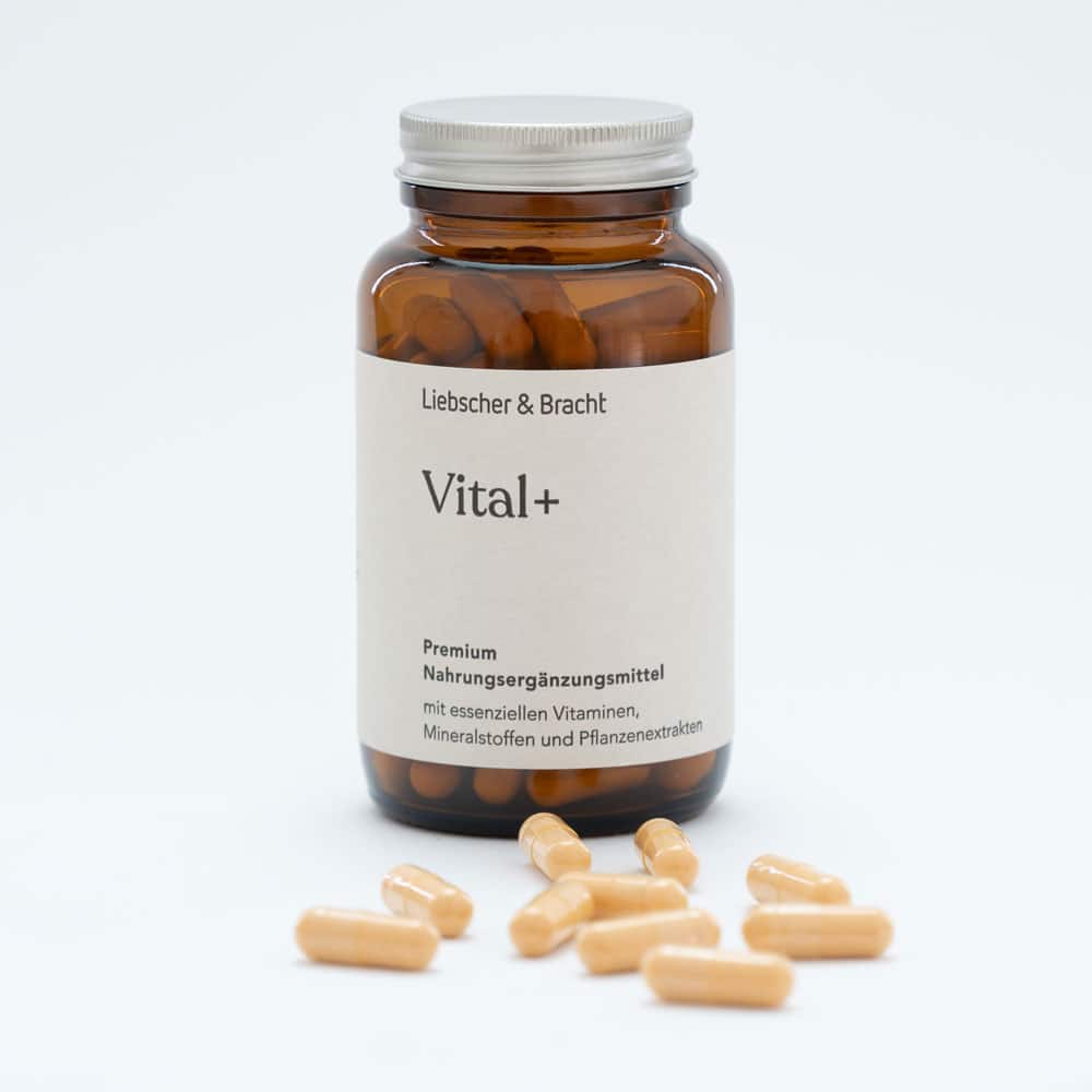 Zu sehen ist eine Braunglasflasche des Nahrungsergänzungsmittels Vital+. Die Flasche ist geöffnet, der Deckel lehnt an der Flasche und einige Nahrungsergänzungsmittel liegen vor der Flasche.