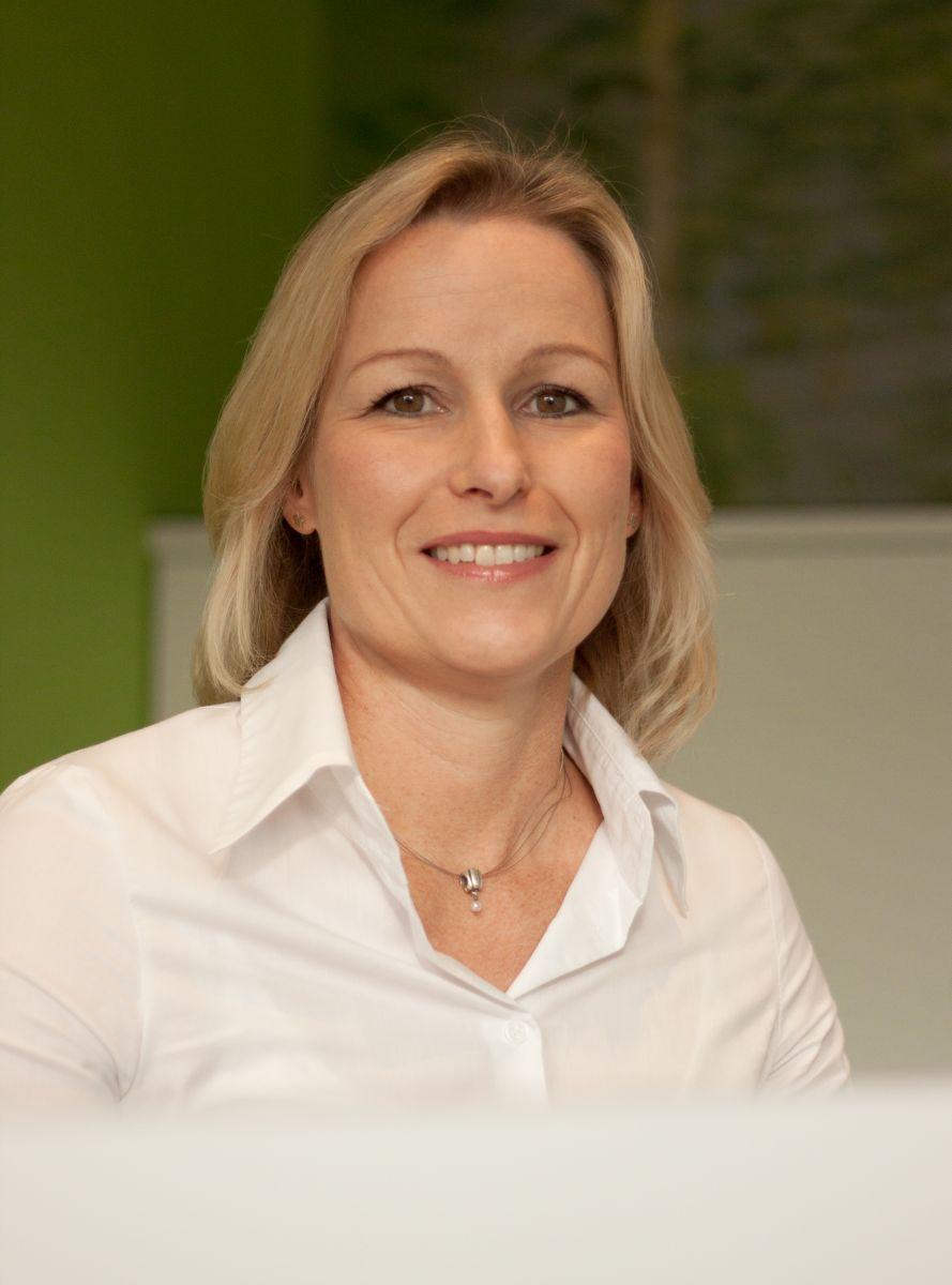 Petra Meyer, Physiotherapeutin aus 49191 Belm, sitzt vor einem grün weißen Hintergrund. Sie hat blonde mittellange Haare und trägt auf dem Foto eine weiße Bluse und eine silberne Kette.