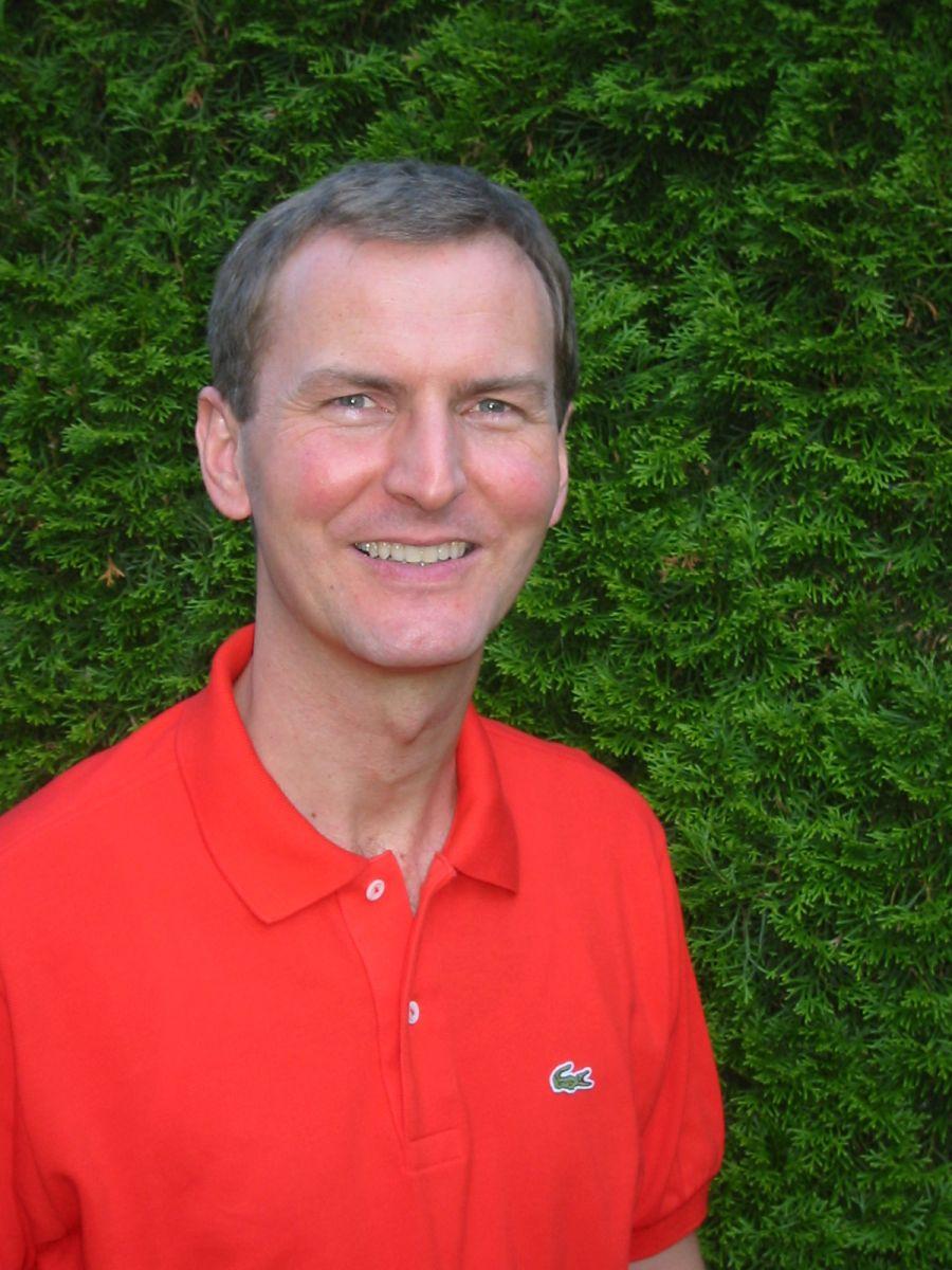 Das Foto zeigt den Heilpraktiker Siegfried Mendler vor einem grünen Busch. Er lacht in die Kamera und hat kurzes braun graues Haar. Auf dem Foto trägt er ein rotes Polo T-Shirt.