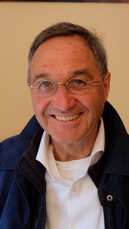 Auf dem Foto steht Werner Zaugg aus Arnstein / Binsfeld vor einem gelben Hintergrund. Er hat dunkelgraue Haare und trägt eine silberne runde Brille sowie ein weißes Hemd und eine blaue Jacke. Er lacht in die Kamera.