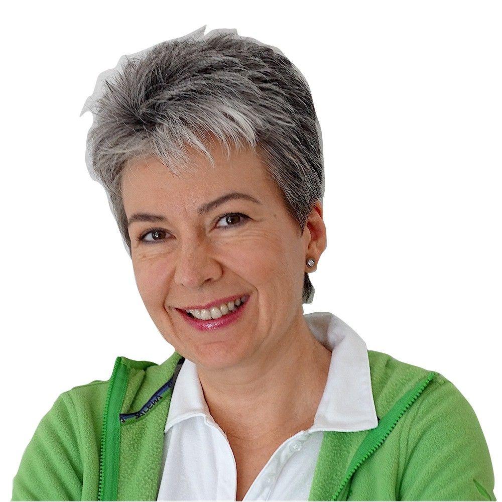 Bettina Mangold aus Stuttgart sieht man lachend vor einem weißen Hintergrund. Sie hat kurze schwarz graue Haare und trägt dazu ein weißes T-Shirt und eine grüne Strickjacke.