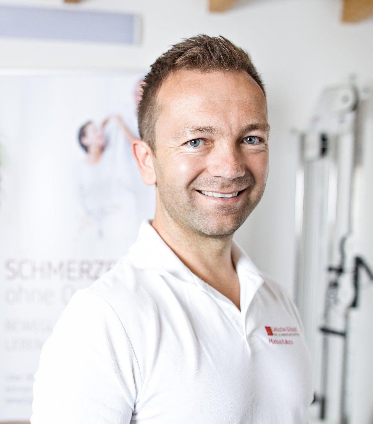 Das Foto zeigt Markus Kaluza vor einem weißen Hintergrund. Er lacht in die Kamera und hat kurzes braunes Haar. Zu dem trägt er ein weißes Polo T-Shirt mit einem schwarzen Logo.