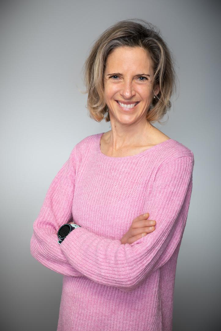 Auf dem Foto leuchtet die Sonne von der Seite auf Nicole Bretting aus Hohenwart. Sie lacht in die Kamera und trägt ihre roten Haare kurz und ein weißes Sport Top.