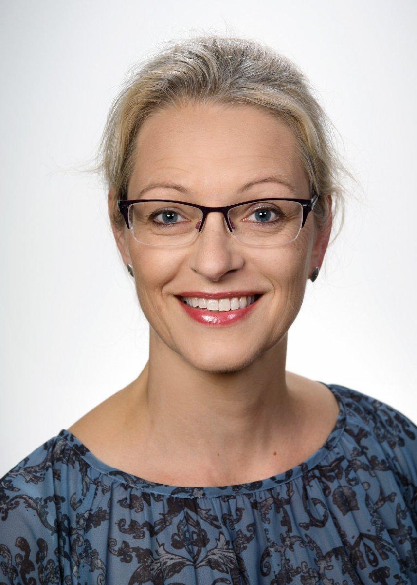 Im Portraitfoto ist Dr. med. Miriam Scheidthauer frontal mit blonden Haaren, Brille und gefleckter, blauer Bluse zu sehen.