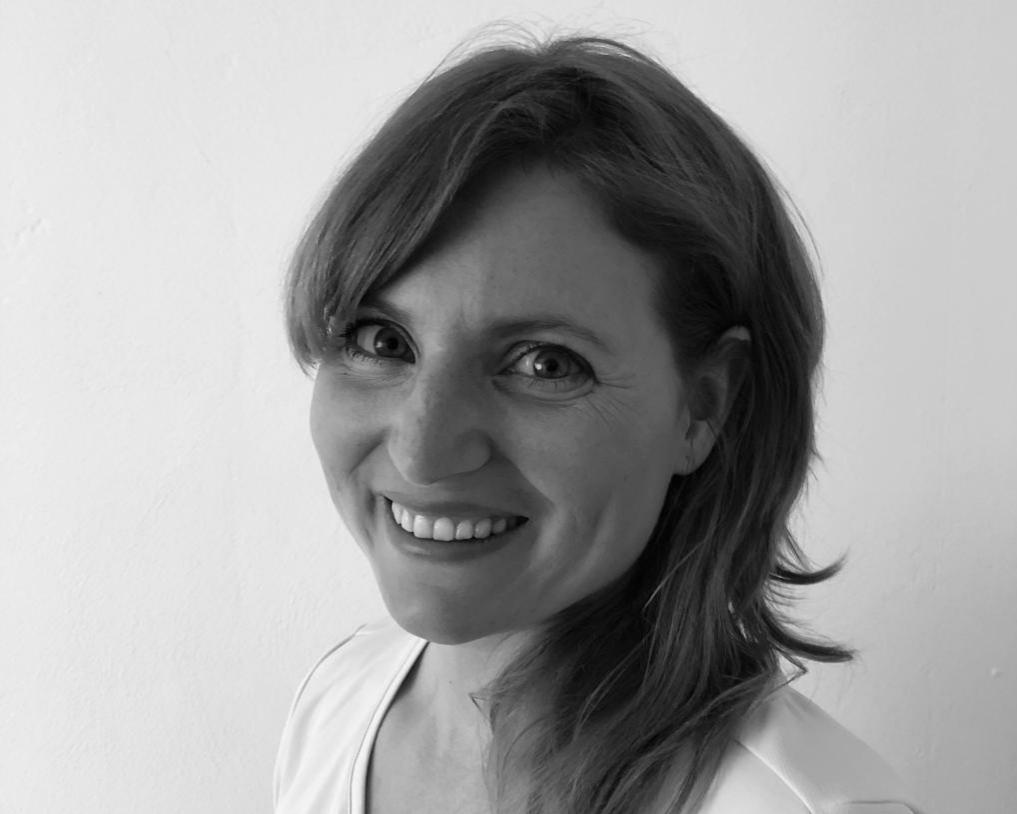 Das schwarz-weiß Portraitfoto zeigt Marie Christin Klein. Sie hat lange braune Haare und einen schrägen Pony. Auf dem Foto schaut sie schräg in die Kamera und lacht.