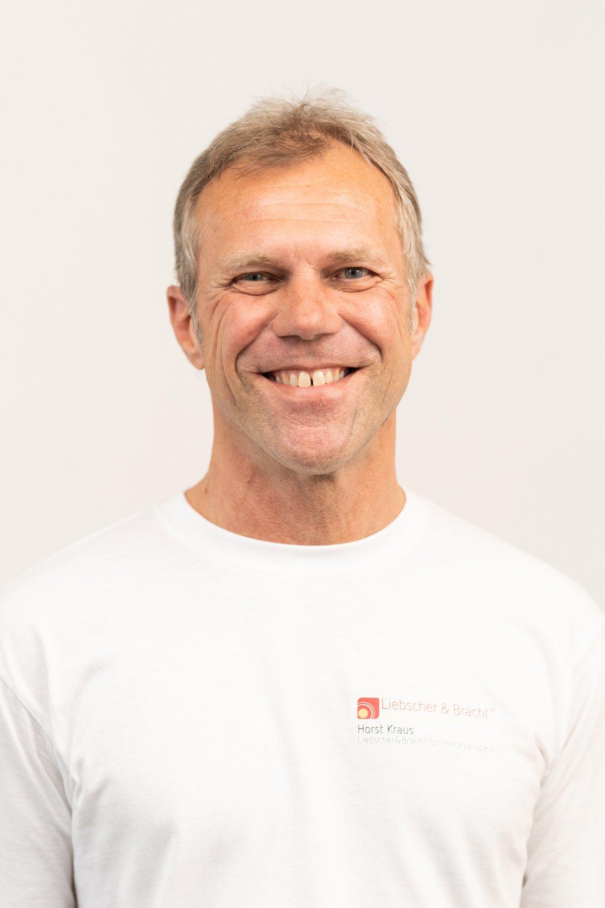 Horst Kraus, Heilpraktiker und Schmerztherapeut aus Forchheim, steht vor einem weißen Hintergrund. Er hat kurze graue Haare und trägt ein Liebscher & Bracht T-Shirt.