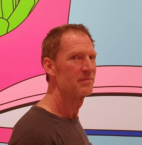 Das Foto zeigt Jors Bruseker aus Aachen vor einem bunten Hintergrund. Er hat kurzes braunes Haar und schaut seitlich in die Kamera. Auf dem Foto trägt er ein braunes T-Shirt.