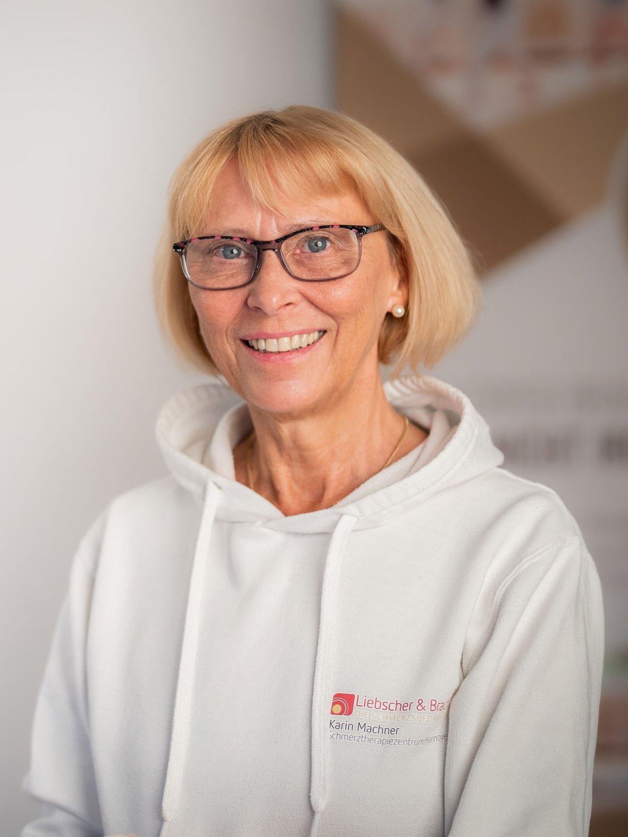 Das Foto zeigt die Physiotherapeutin Karin Machner aus Hannover. Sie hat blonde mittellange Haare und einen Pony. Auf dem Foto trägt sie ein weißes T-Shirt und eine schwarze Perlenkette.