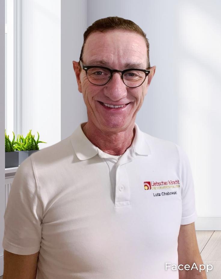 Lutz Chabowski hat kurze braune haare und eine schwarze Brille. Im Hintergrund des Therapeuten aus Erlangen befindet sich ein Raum mit Menschen.