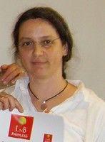 Das Foto zeigt Riek Rohland aus Kaiserslautern. Sie trägt ihre langen braunen Haare als Zopf und eine randlose Brille. Dazu ein weißes Polo T-Shirt und eine schwarze Kette. Am unteren Bildrand hält sie Ihre Urkunde der L&B Ausbildung hoch.