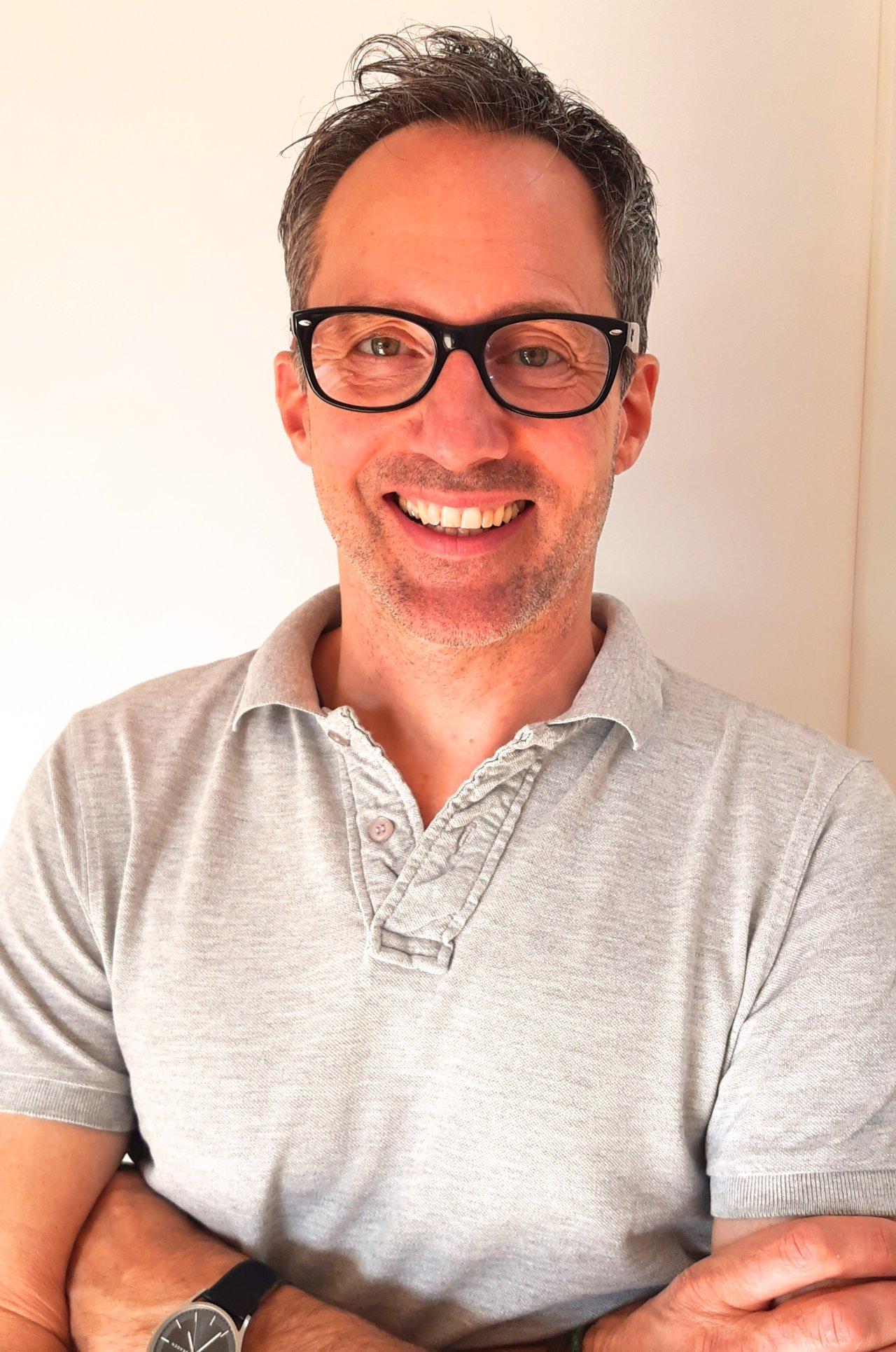 Das Foto zeigt den Heilpraktiker für Physiotherapie Stefan Kühn aus Bietigheim-Bissingen, der in die Kamera lächelt. Er hat kurze braune Haare und trägt eine eckige schwarze Brille und ein Liebscher & Bracht Polo T-Shirt.