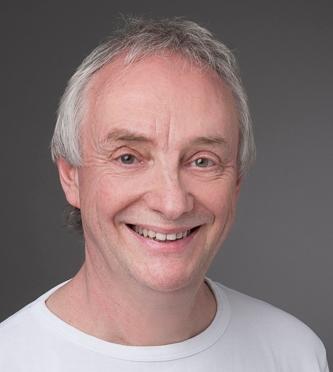 André Henzmann hat hellgraue Haare und trägt ein weißes T-Shirt. Das Portraitfoto ist vor einem grauen Hintergrund aufgenommen worden