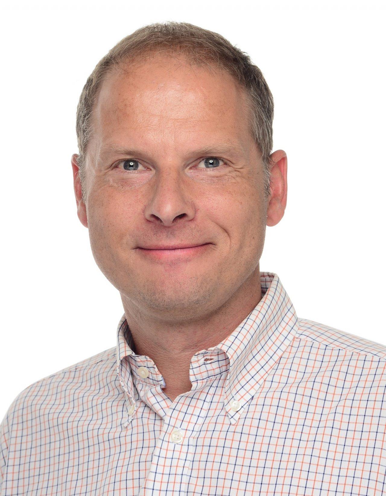 Das Foto zeigt den lächelnden Heilpraktiker Dirk Peretzki. Dieser trägt ein weißes Liebscher & Bracht Polo T-Shirt und hat kurze braune Haare.